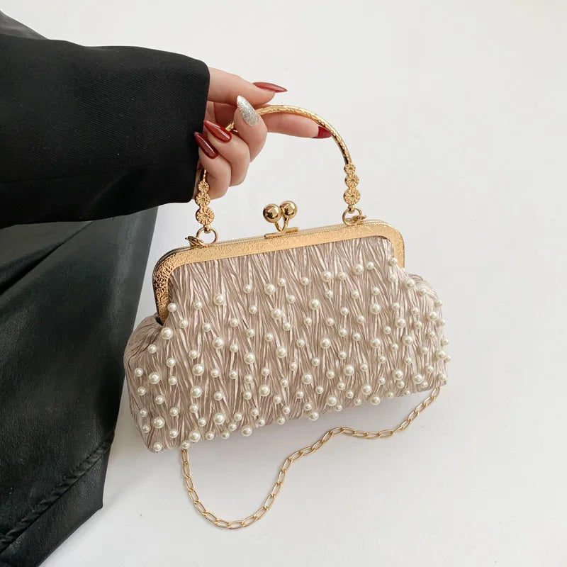 A beige pearl embellished crossbody shoulder bag held by a hand wearing red nail polish.