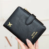 A hand holds a black leather travel wallet with a gold zipper and a gold airplane emblem.