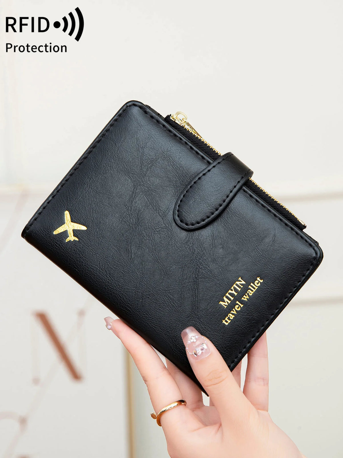 A hand holds a black leather travel wallet with a gold zipper and a gold airplane emblem.