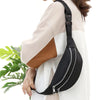 A black nylon crossbody sling bag is worn on a person's shoulder, featuring a zipper closure.