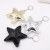 Three star-shaped leather keychains in gold, silver, and black with metal jump rings