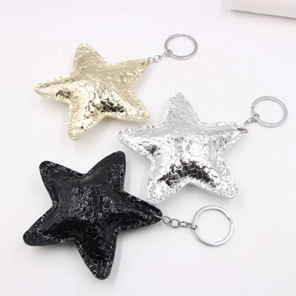 Three star-shaped leather keychains in gold, silver, and black with metal jump rings