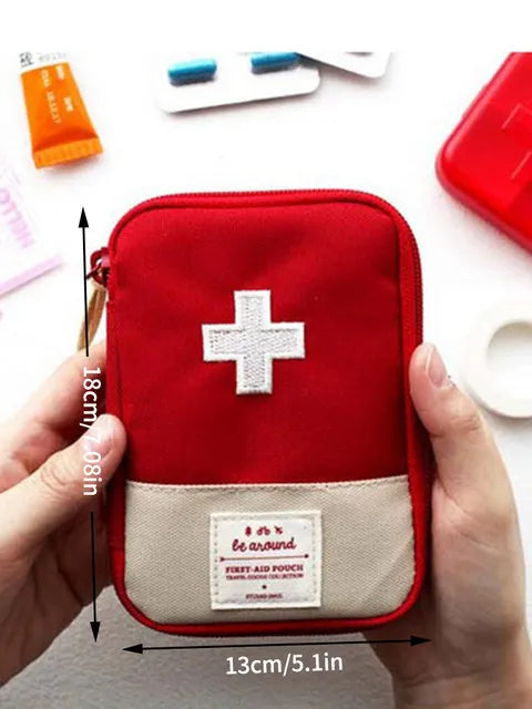 A red pouch containing a white cross first aid kit is held by a hand, showing its size.