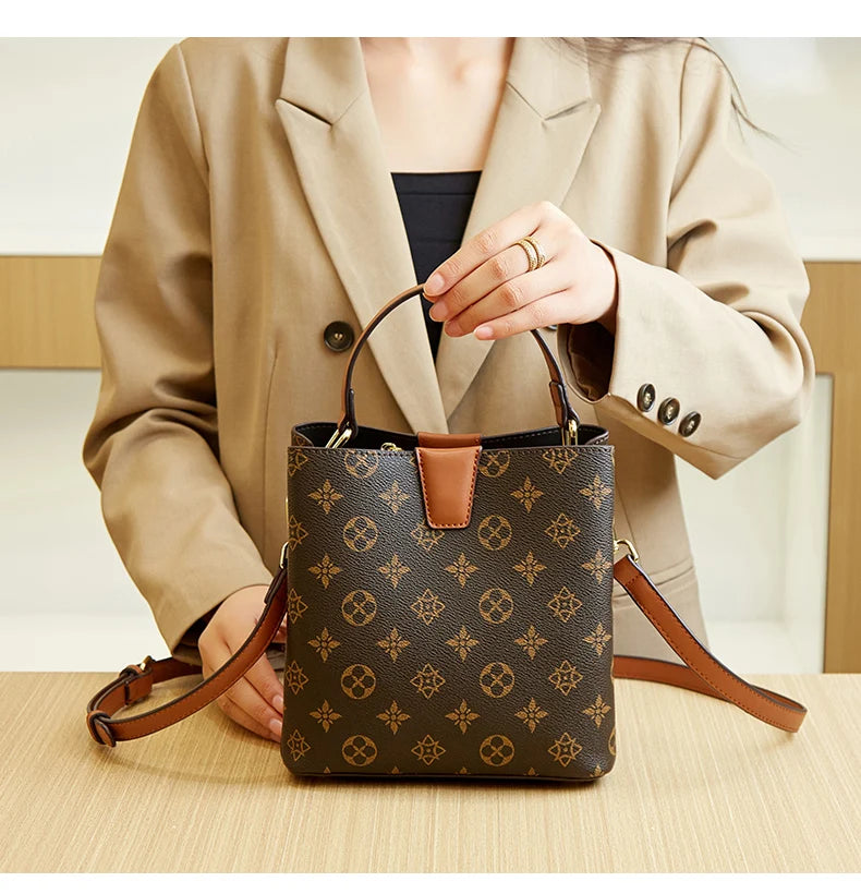 A woman holds a brown leather bucket bag with a floral pattern against a light background.