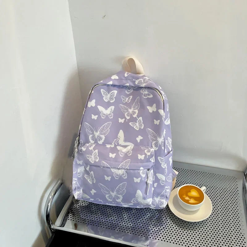 A purple backpack with a white butterfly pattern resting on a metal shelf next to a cup of tea.