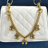 Collar de cadena de oro con adornos de cereza sobre un bolso de cuero blanco acolchado.