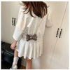 A woman models a light gray acrylic bow clasp mini handbag with a gold chain strap against a white wall.