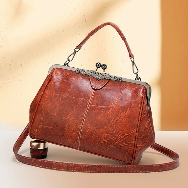 A brown leather crossbody shoulder bag with a silver hardware detail resting on a light surface.
