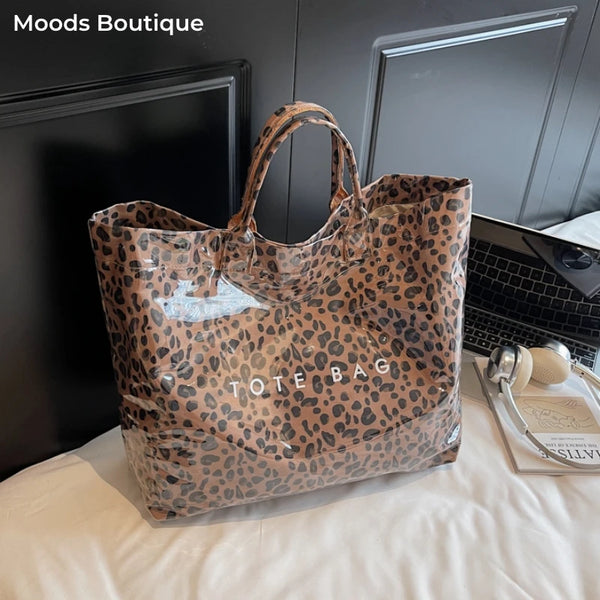A brown leopard print PVC tote bag is displayed on a white cloth next to a laptop.