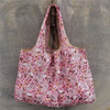 A pink patterned reusable shopping bag hanging from a wooden hanger against a gray background.