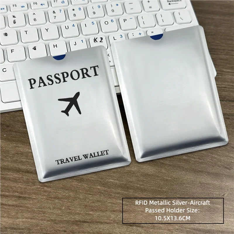 Silver RFID metallic passport holder with an airplane design placed on a wooden desk next to a laptop keyboard.