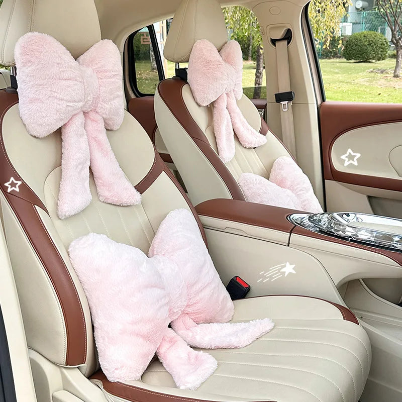 Interior view of a car seat showing pink bowknot headrest pillows and beige leather upholstery.