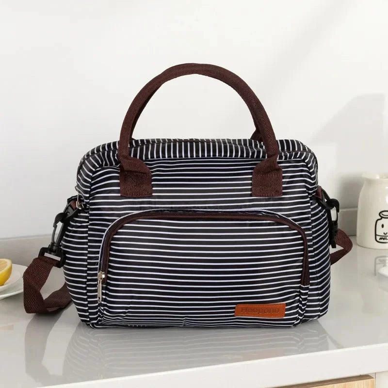 Bolsa térmica portátil a rayas blanco y negro con asas y ribetes marrones sobre una superficie blanca.