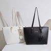 Bolso de hombro de cuero sintético negro con un dije dorado y un pompón negro colgando de la correa.