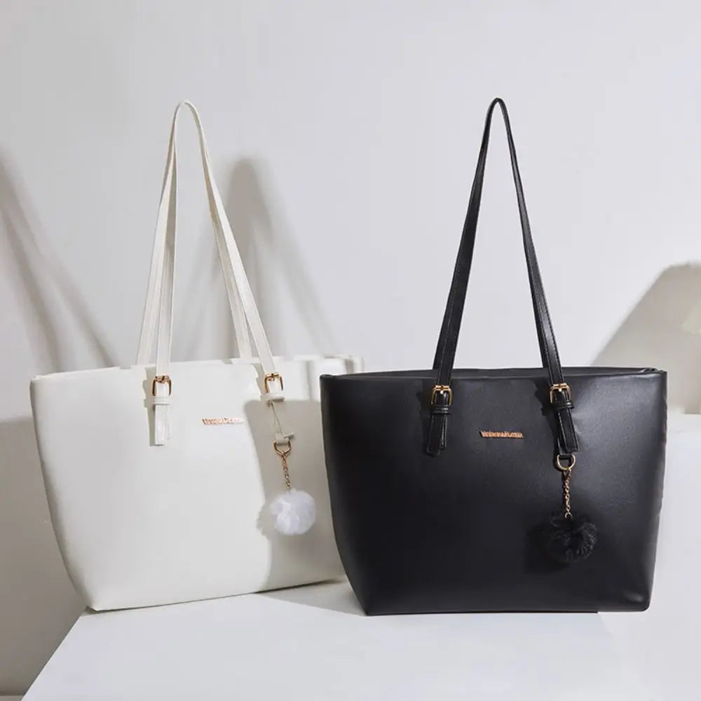 Bolso de hombro de cuero sintético negro con un dije dorado y un pompón negro colgando de la correa.