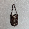 A dark brown beaded clutch bag hanging by a thin string against a light gray, speckled background.
