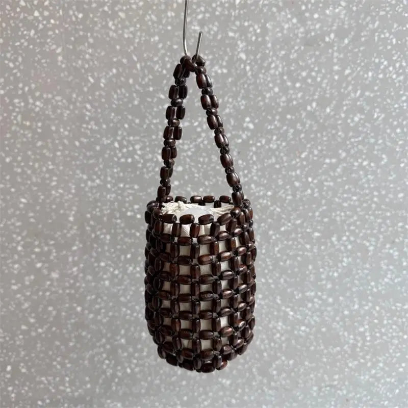A dark brown beaded clutch bag hanging by a thin string against a light gray, speckled background.