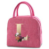 A pink insulated canvas lunch bag with a gold letter T print and pink straps.