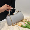 A hand holds a silver glitter crossbody evening clutch bag with gold chain accents on a white textured surface.