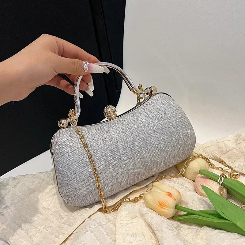 A hand holds a silver glitter crossbody evening clutch bag with gold chain accents on a white textured surface.