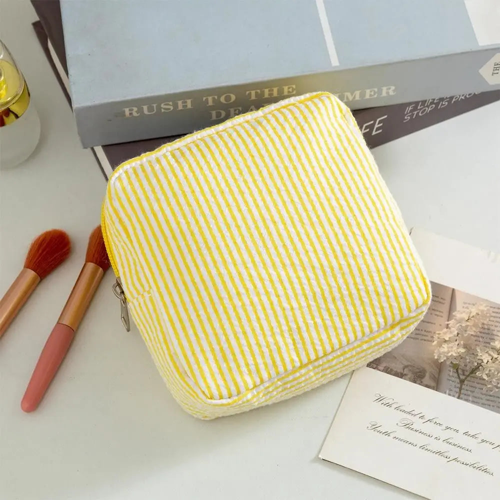 A yellow striped storage pouch is shown next to makeup brushes and a book.