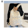 A light cream nylon backpack with a blue bow print is carried by a person against a white background.