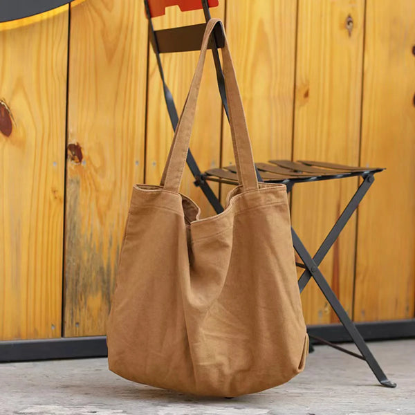 Braune Leinenshultertasche hängt vor einem Holzhintergrund neben einem schwarzen Klapphocker.