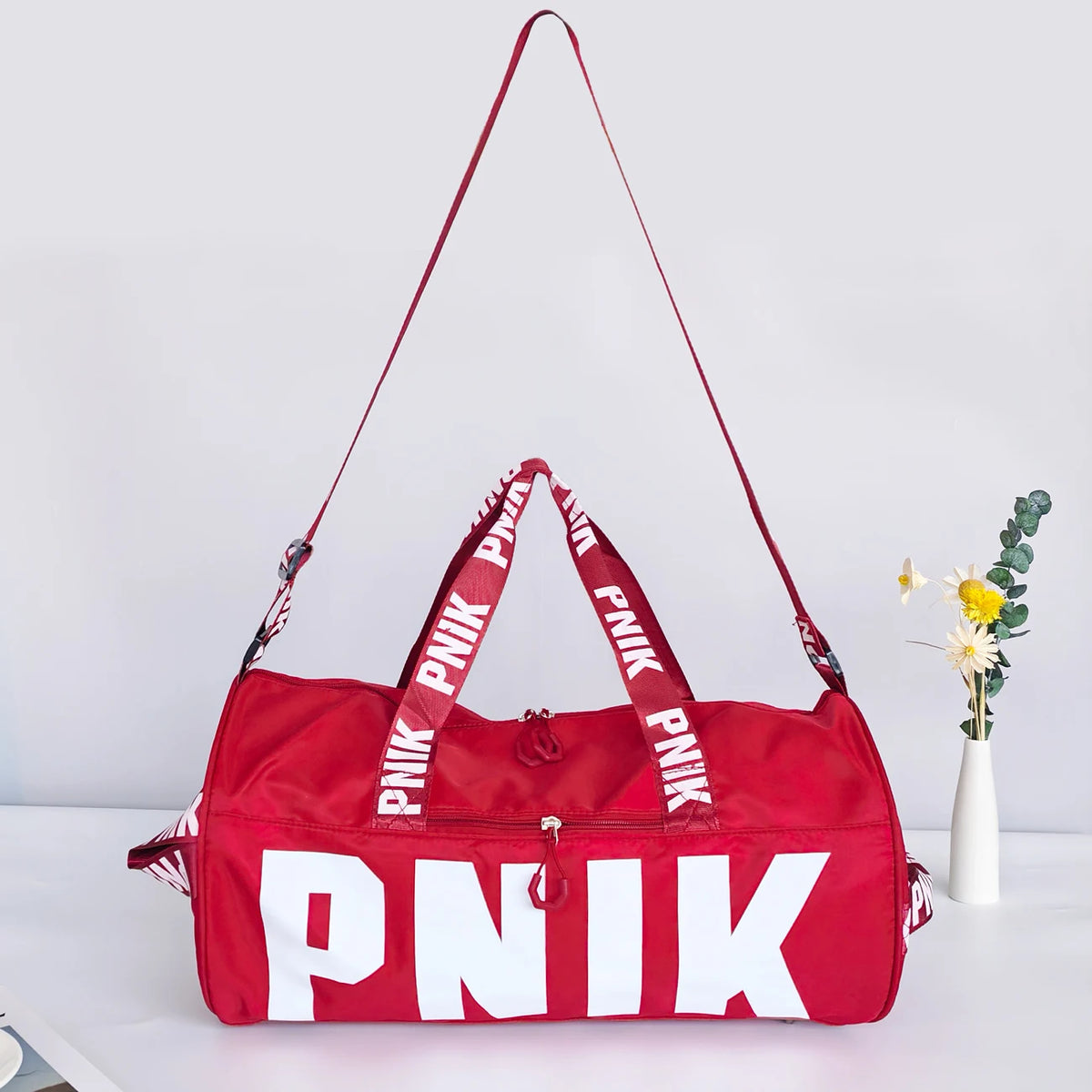 A bright red Nike PNIK shoulder bag with white lettering, shown against a light background.