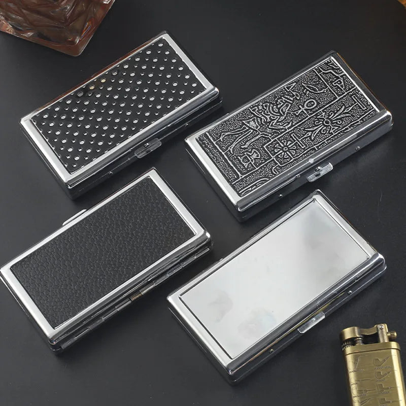 Three metal cigarette case holders with different textures and designs are displayed on a dark surface.