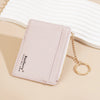 A pale pink ultra-thin card holder wallet with a gold chain is shown resting on a light beige surface.