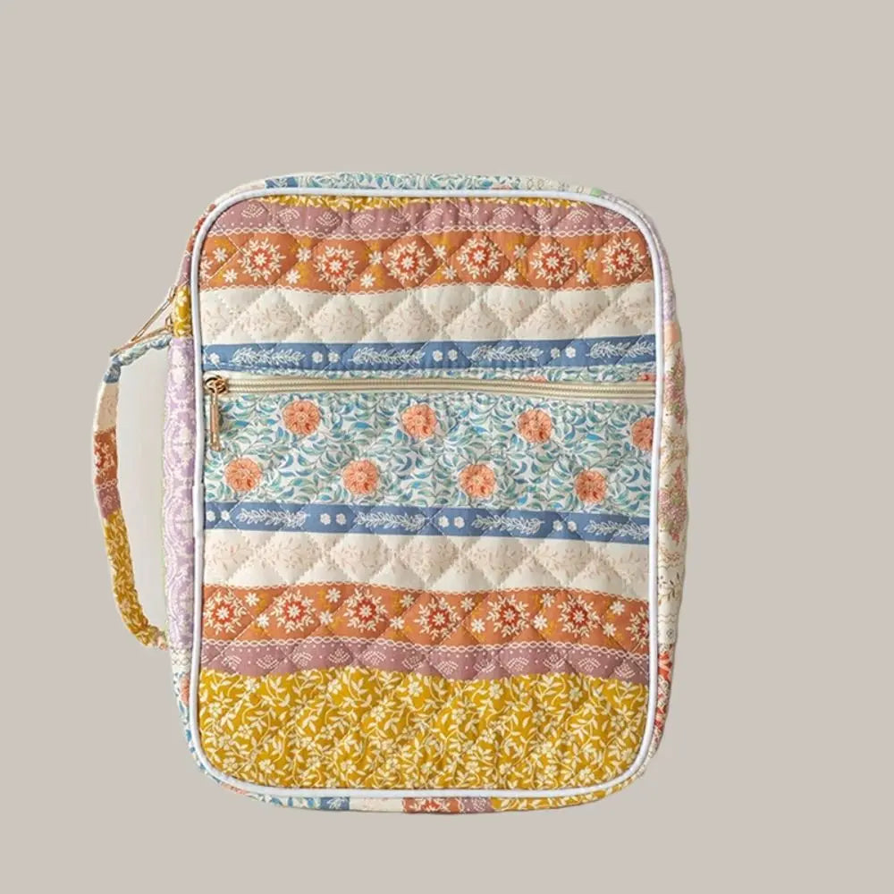 A quilted floral Bible cover in various pastel and earthy tones with a zipper and pen holder.