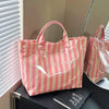 A pink and beige striped tote bag is displayed on a dark surface next to a book.