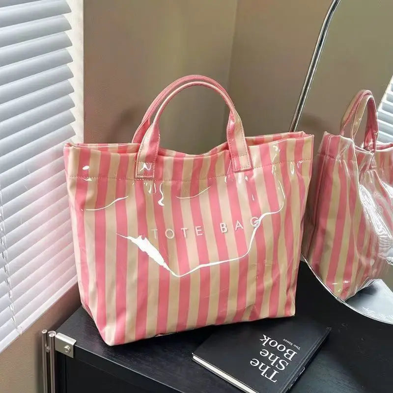 A pink and beige striped tote bag is displayed on a dark surface next to a book.