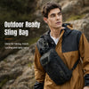 A man wearing a tan and black jacket is holding an outdoor ready sling bag in a natural, rocky outdoor setting.