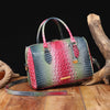 A luxury crocodile pattern crossbody tote bag in green and red leather rests on a wooden surface next to a dried animal bone.