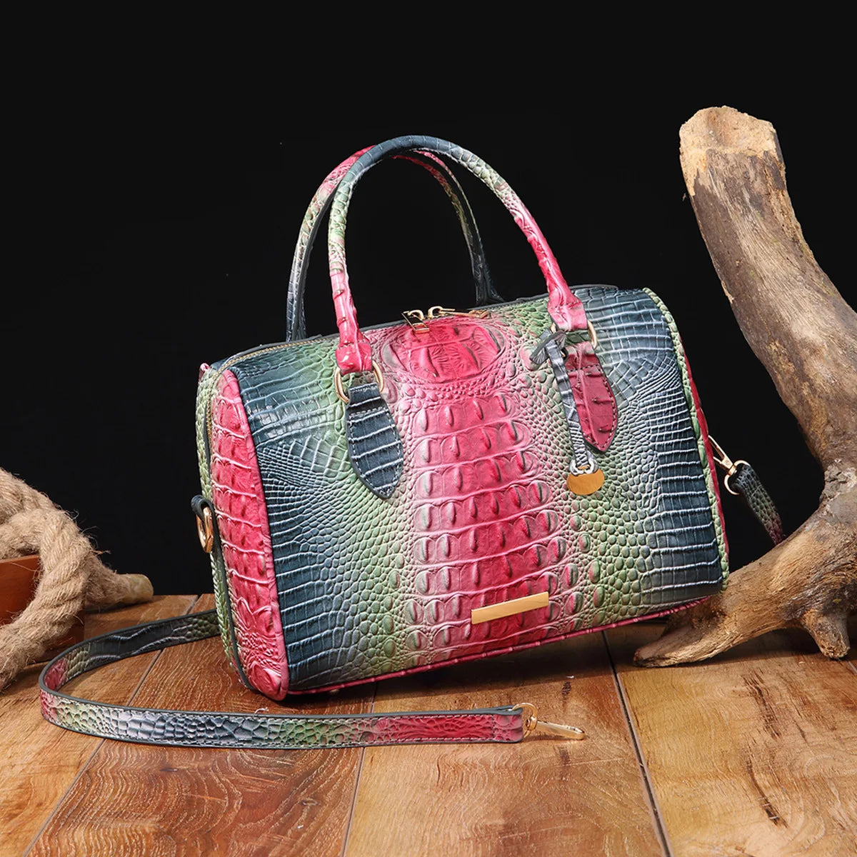 A luxury crocodile pattern crossbody tote bag in green and red leather rests on a wooden surface next to a dried animal bone.