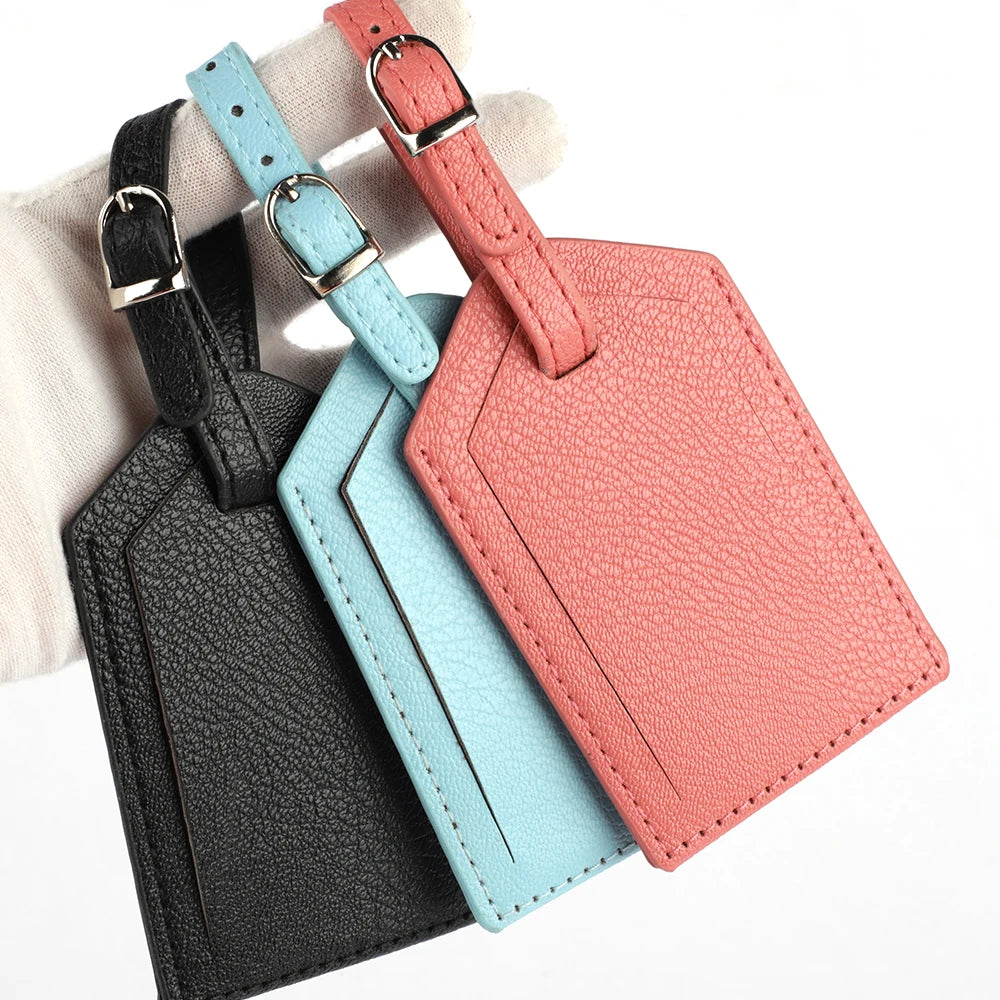 Three pink, blue, and black PU leather luggage tags with silver hardware stacked on a light background.