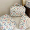 A white quilted floral embroidered makeup bag with blue accents resting on a white surface.