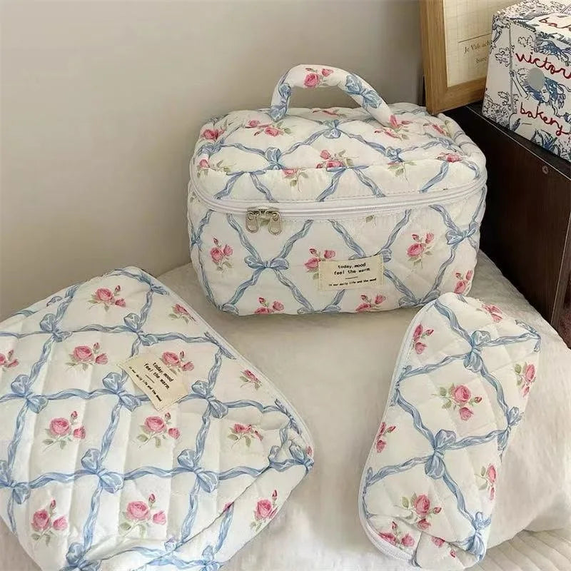 A white quilted floral embroidered makeup bag with blue accents resting on a white surface.