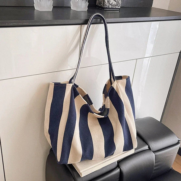 A striped canvas tote bag with a dark blue and beige pattern is displayed on a black cabinet.