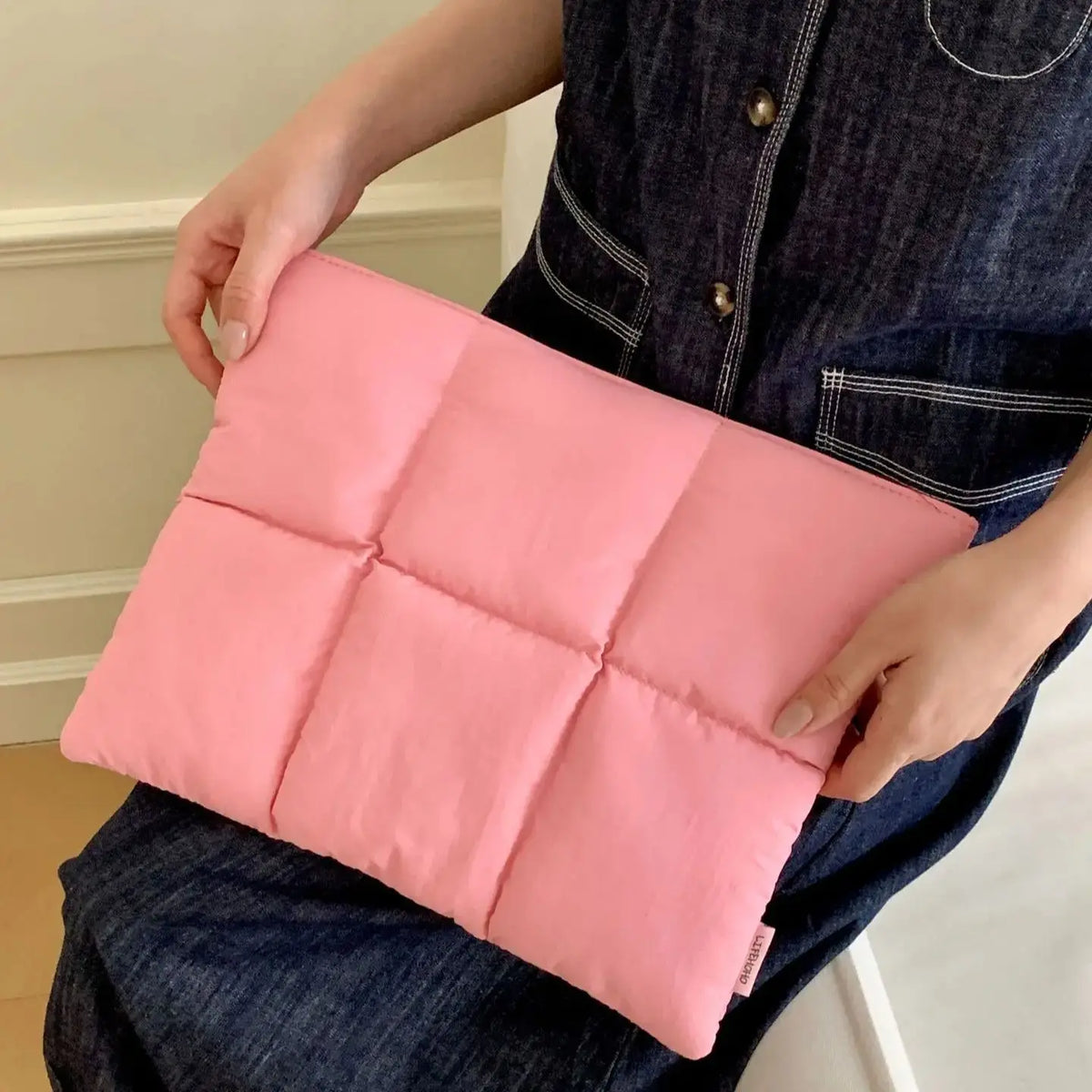 A pink quilted laptop sleeve is being held by a person wearing a dark denim shirt.