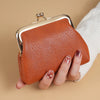 A brown leather coin purse with a gold buckle is held by a hand next to a white knitted sleeve.