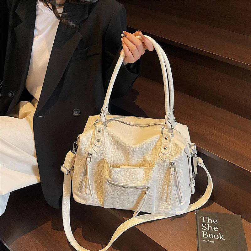 Bolso cruz de cuero suave blanco de lujo sostenido por una mujer con blazer negro.