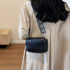 A beige long-sleeved shirt features a black vegan PU crossbody bag with a patterned strap.