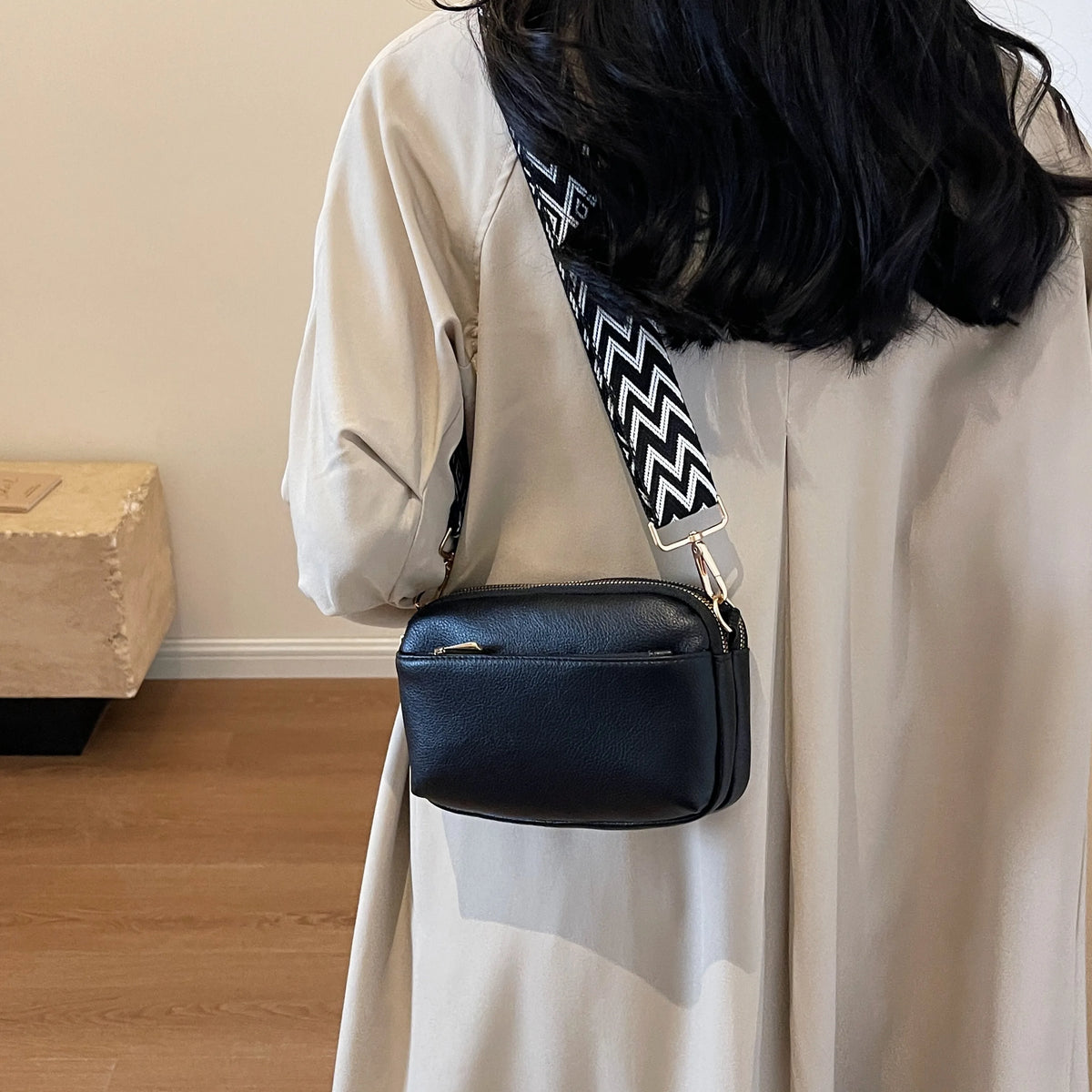 A beige long-sleeved shirt features a black vegan PU crossbody bag with a patterned strap.