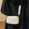 A cream-colored vegan PU crossbody bag with a geometric patterned strap is shown hanging from a black coat.