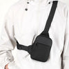 A black canvas crossbody sling bag is attached to the front of a white jacket.