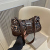 Un sac à main en cuir faux léopard marron avec une bretelle, tenu sur un fond clair.