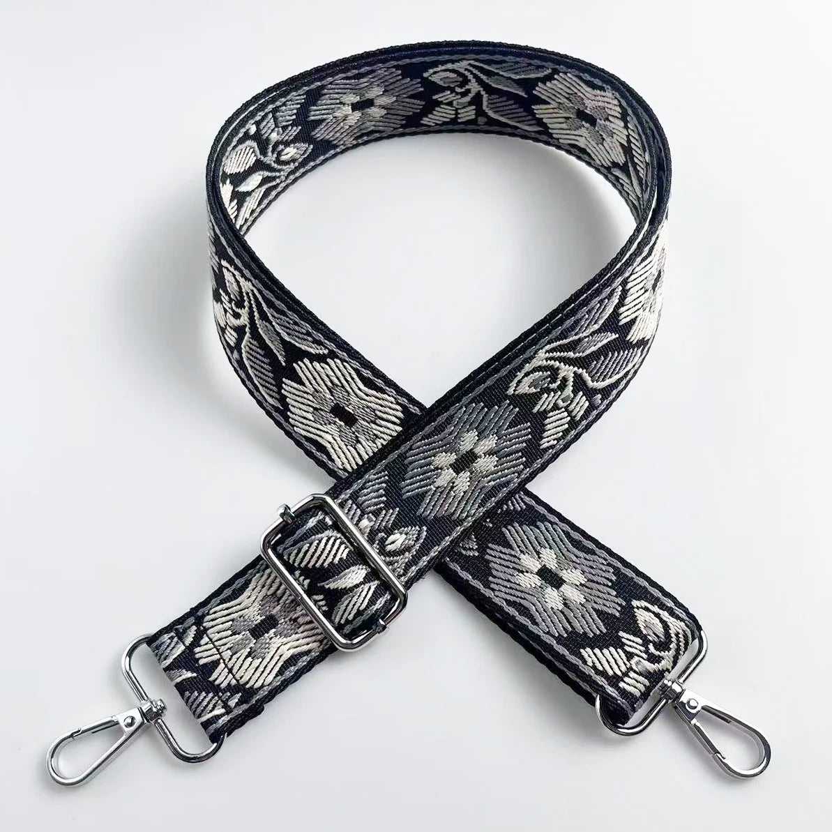 A black and white floral jacquard strap for a crossbody bag, featuring an adjustable buckle.