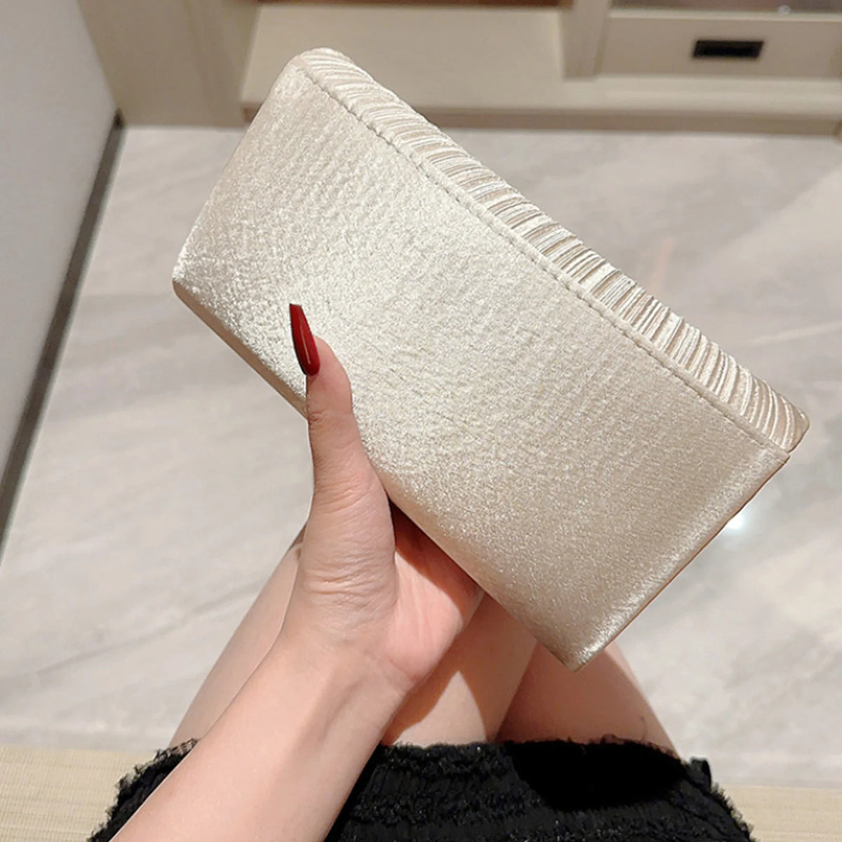 A hand holds a beige luxury chain shoulder clutch bag with a textured finish.